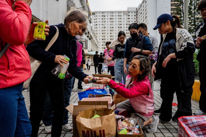 Displaced residents from an apartment fire gather outdoors as a woman distributes food and drinks among a group of people