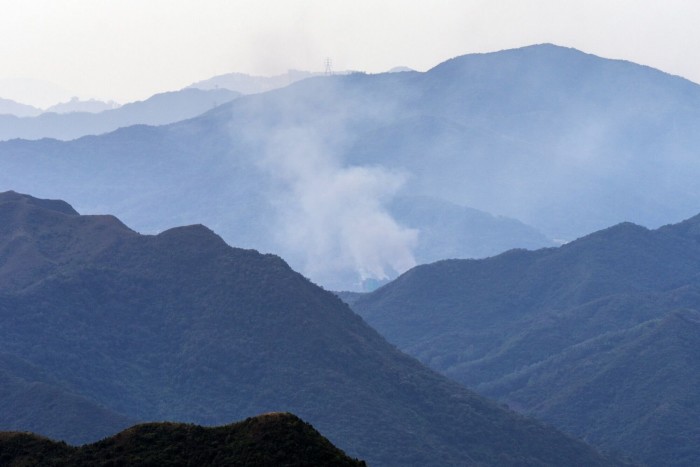Smoke billows from between mountain ridges, rising from the fire at a high-rise complex in the distance.