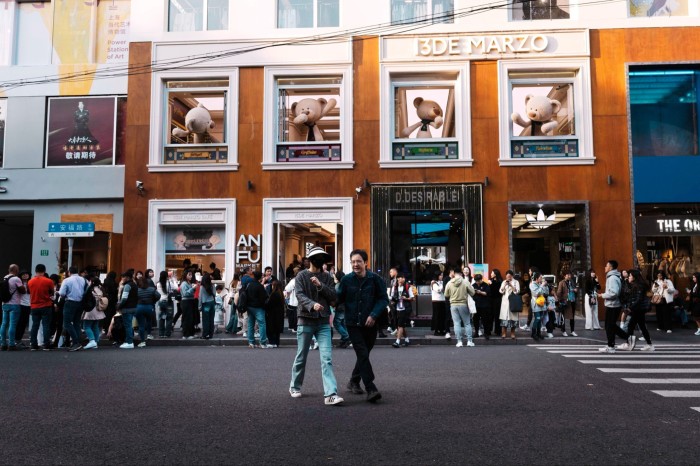 Crowds of people walk and gather outside shops on a busy street in Shanghai, with large teddy bears displayed in upper windows.