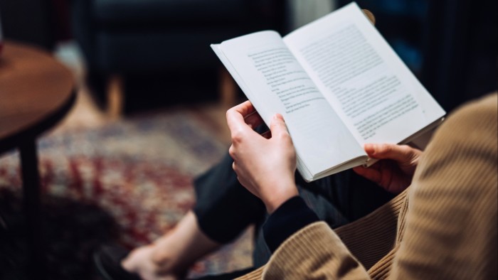 Woman sitting on a sofa in a cosy room, holding an open book in her hands.