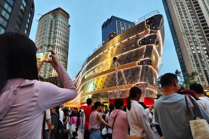 Crowds gather in front of a ship-shaped Louis Vuitton flagship store in a busy Shanghai shopping district