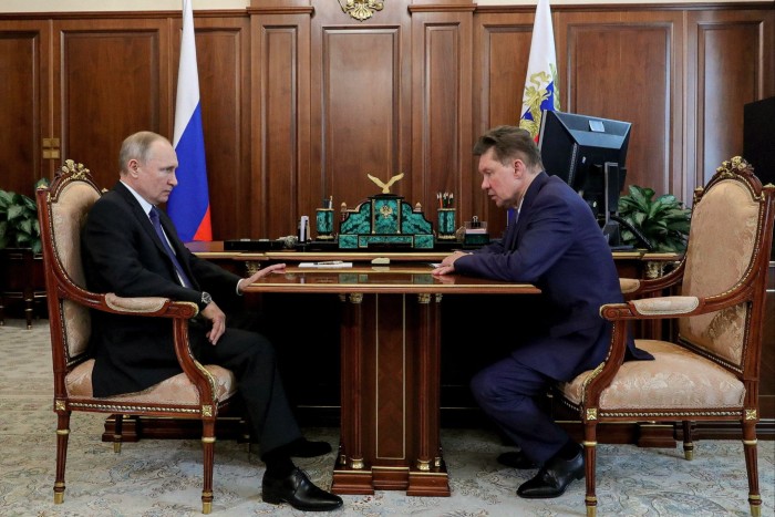 Vladimir Putin and Alexei Miller sit across from each other at a wooden desk during a meeting at the Kremlin.