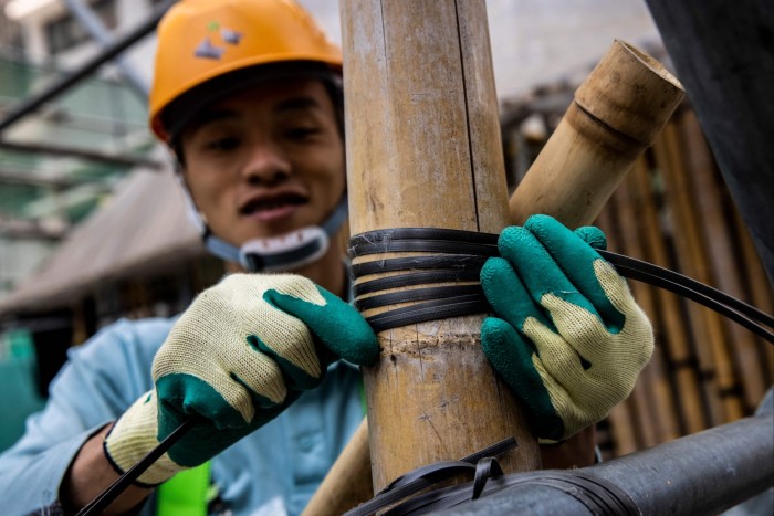 A worker wearing a hard hat and gloves, ties bamboo poles together during a bamboo scaffolding class in Hong Kong.