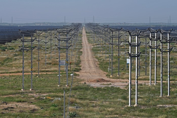 Rows of solar electric lines and transmission poles stretch into the distance at Bhadla Solar Park amid dry, grassy terrain.
