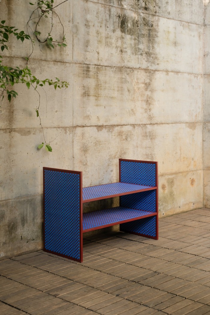 A small shelving unit with blue and red checkered panels stands on a wooden floor against a weathered concrete wall.
