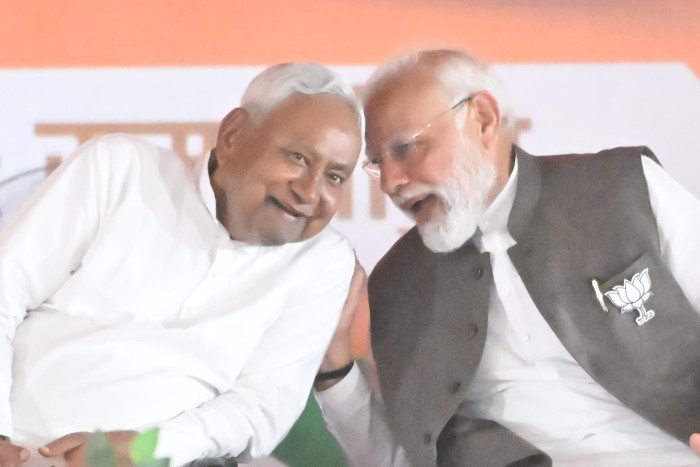 Modi speaks closely with Kumar as both smile during a public meeting.