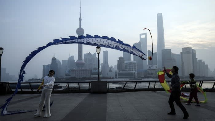 A person flies a blue dragon-shaped kite on the Bund with Shanghai’s Lujiazui skyline, including the Shanghai Tower, in the background.