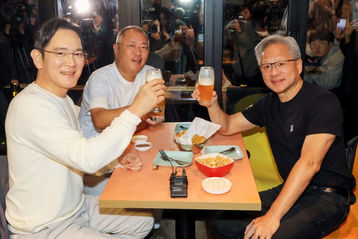 Jensen Huang, Jay Y. Lee, and Euisun Chung raise glasses of beer together at a restaurant table with fried chicken and snacks.