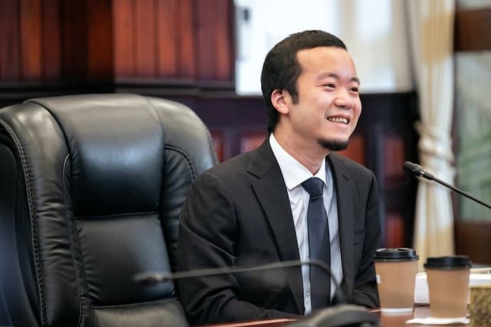 Chen Zhi, chair of Prince Group, smiling while seated at a conference table with two coffee cups in front of him.