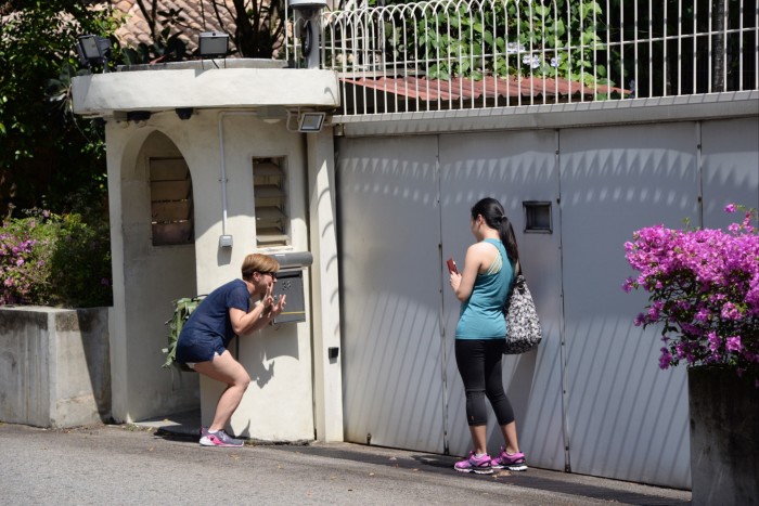 Two women stand outside the gate of 38 Oxley Road, with one crouching near the mailbox and the other holding a phone.