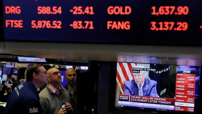Traders on the New York Stock Exchange floor watch a screen showing President Donald Trump speaking, with declining market figures displayed above.