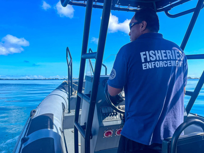 Alt text for image 4: A fisheries enforcement officer steers a patrol boat across the flat open ocean on a clear day.