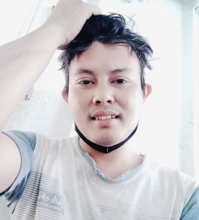 Alt text 1: Portrait of Deby Putra Bunanda smiling and looking at the camera, wearing a light shirt with one hand placed on his head.