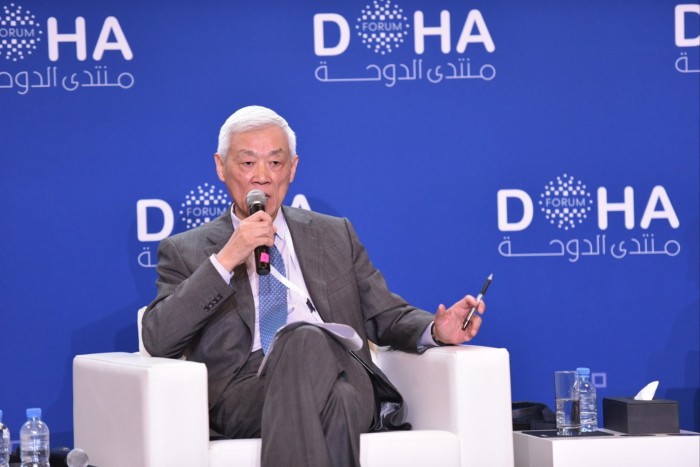 Zhang speaks into a microphone while seated on stage at a forum in Doha.