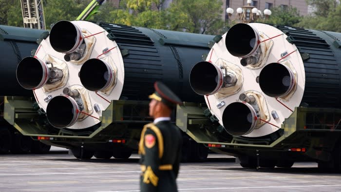 A member of the People's Liberation Army stands in front of large DF-5C nuclear missiles mounted on military vehicles during a parade.
