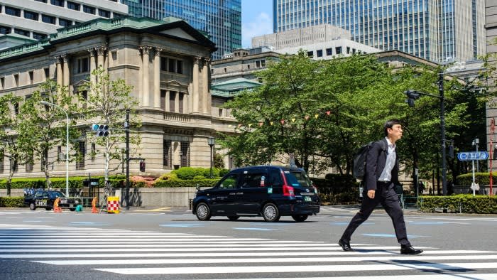 A man in a suit with a backpack crosses a street in front of the Bank of Japan building in central Tokyo.