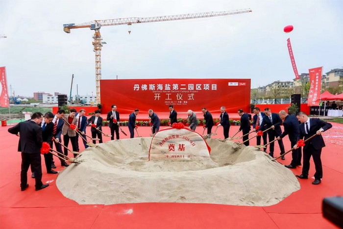 A group of people in business attire participate in a ceremony, shoveling sand in front of a red backdrop for the Danfoss Haiyan Second Campus Project