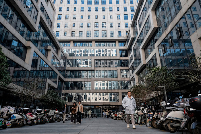 People walk between lines of parked scooters outside the Hongshan AI building in Wuhan.