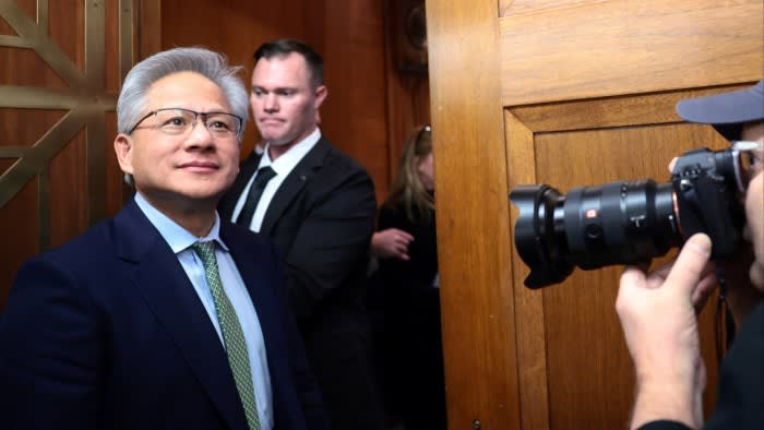 Jensen Huang stands in a hallway, looking ahead, as a photographer takes his picture.