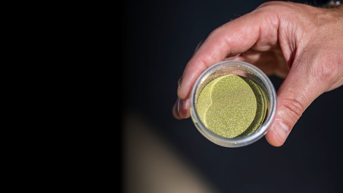 A hand holds a clear container filled with fine, yellowish diamond grit