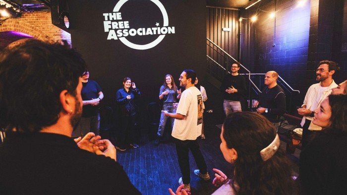 A group of people stand in a circle, laughing and participating in an improv class warm-up at The Free Association venue
