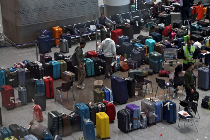 Rows of unclaimed suitcases and bags are lined up inside an airport terminal as staff and passengers move among them