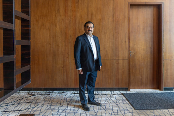 Gautam Adani stands in a suit against a wooden-paneled wall at the Adani Group headquarters.