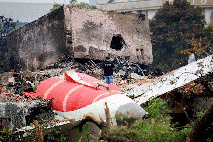 A firefighter stands near the wreckage of an Air India Boeing 787-8 Dreamliner among debris and a damaged building.