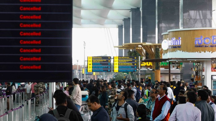 Travellers look at a flight information screen displaying several cancelled and delayed flights by IndiGo airlines