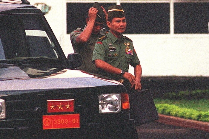Prabowo Subianto, in military uniform, walks beside a vehicle at army headquarters, followed by an unidentified adjutant.