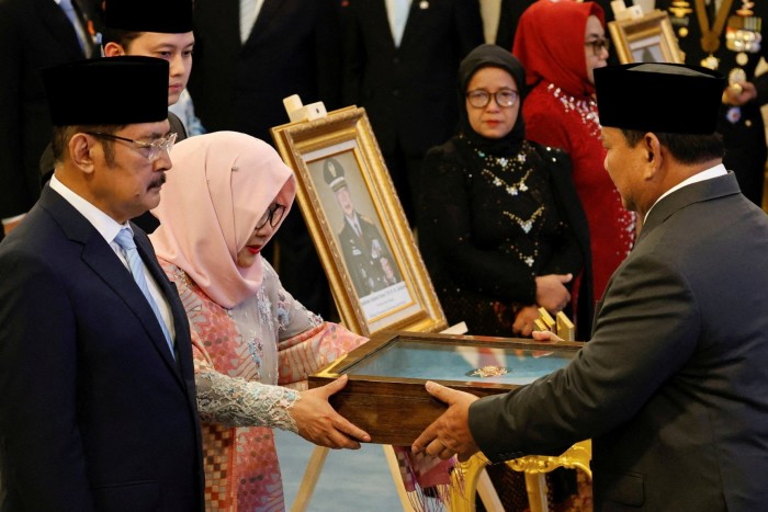 Prabowo Subianto hands a plaque to Siti Hardijanti Rukmana during a ceremony honoring Suharto as a national hero.
