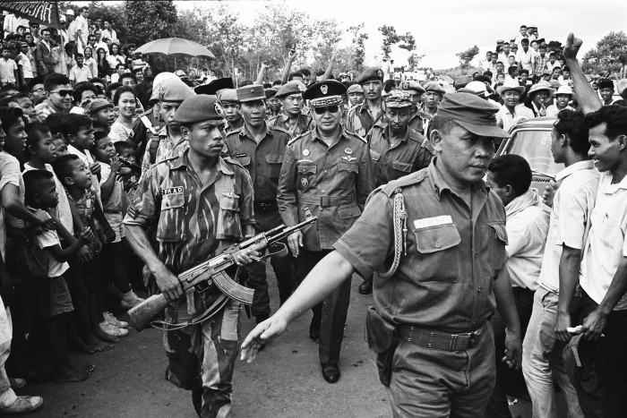 Defense Minister Suharto walks with military personnel through a crowd at the state funeral of Sutan Sjahrir.