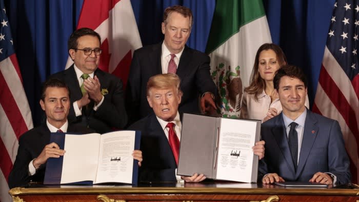 Enrique Pena Nieto, Donald Trump, and Justin Trudeau sit holding signed USMCA documents, with Ildefonso Guajardo Villarreal, Robert Lighthizer, and Chrystia Freeland standing behind them.