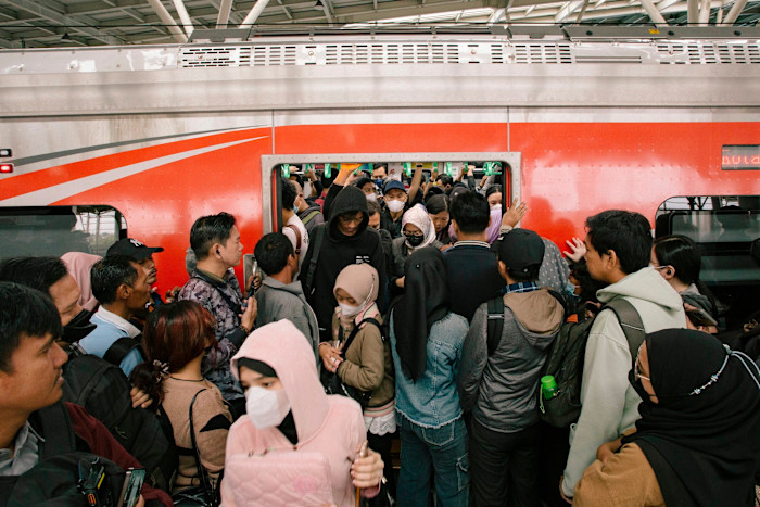 Crowd of commuters, many wearing masks, squeeze onto a packed train at Manggarai station during morning rush hour.
