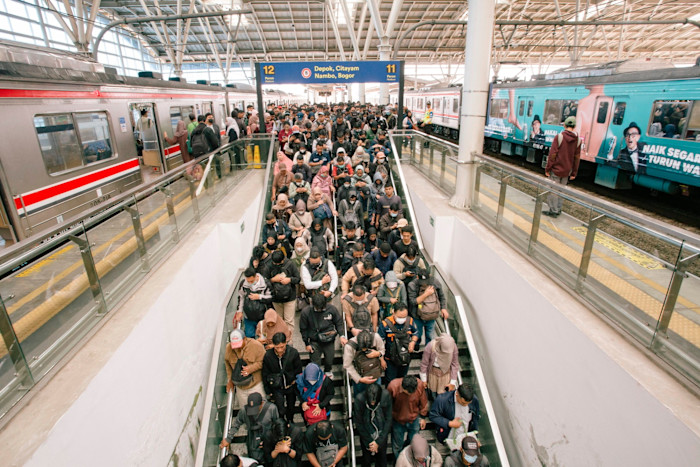 A large crowd of commuters descends an escalator between two trains at Manggarai station during morning rush hour.