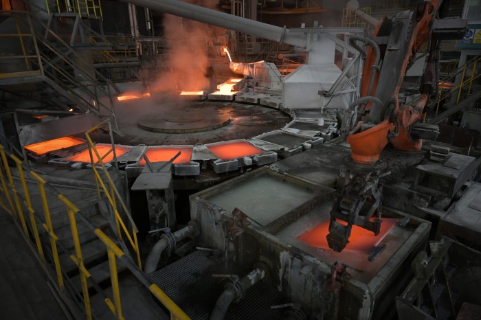 A robotic arm lifts a glowing copper cathode sheet into a cooling bath at a copper smelting plant. Steam rises from the molten metal.