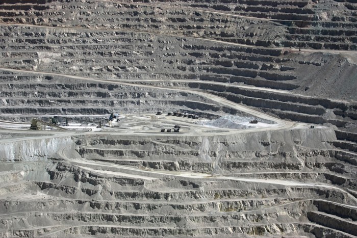 Aerial view of the terraced, open-pit Escondida copper mine with mining trucks and equipment visible on the mine floor.