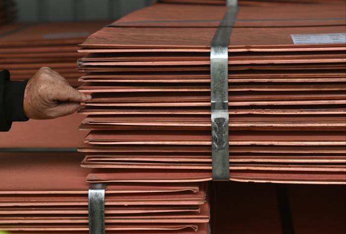 Stacks of copper cathode sheets secured with metal bands, with a person’s hand inspecting the edges.