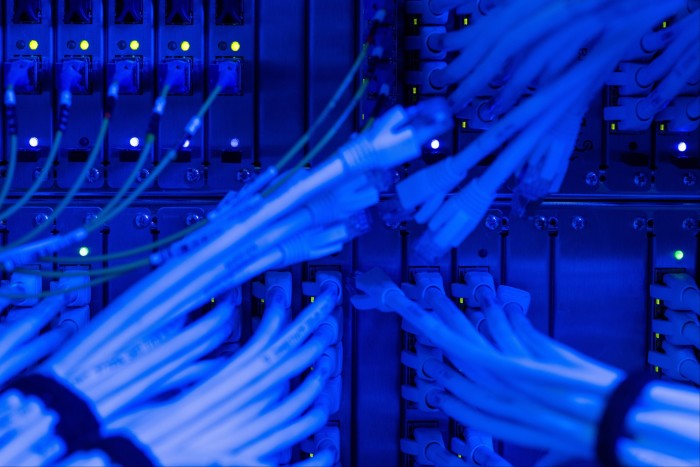 Bundles of fiber optic and Ethernet cables plugged into switches, illuminated by blue LED lights inside a communications room.