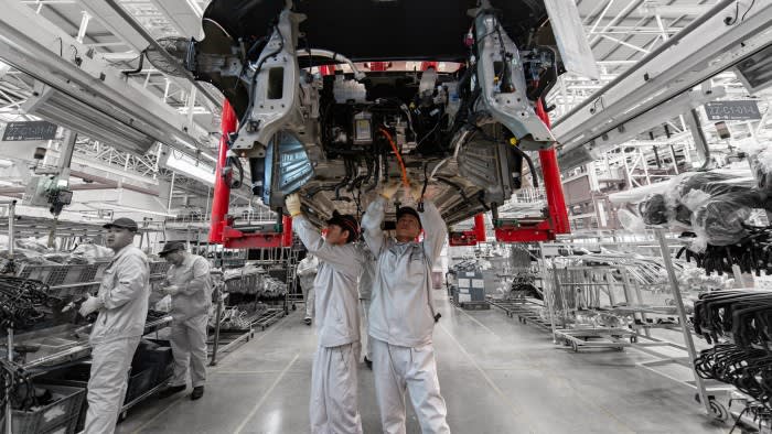 Factory workers reach up to work on a car above their heads on a production line