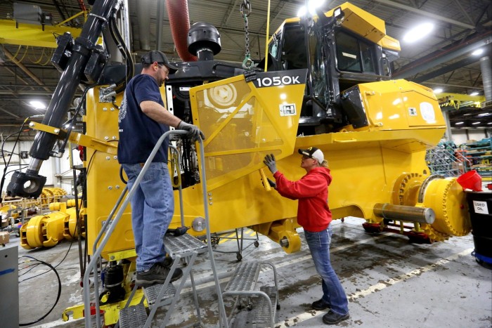 Rick Ring and Corinne Schmitt-Bries attach a panel to a John Deere 1050K Crawler Dozer inside a factory.