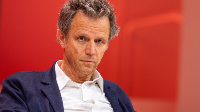 Arthur Sadoun appears seated against a red background, wearing a white shirt and navy blazer at the VivaTech conference.
