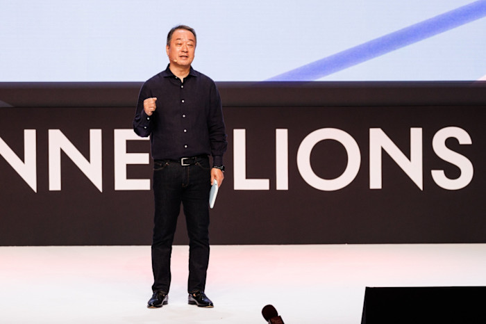 Hiroshi Igarashi speaks onstage, holding a paper and gesturing with his right hand during a Cannes Lions session.