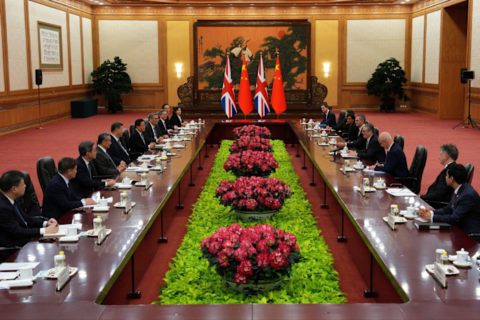 Sir Keir Starmer and Xi Jinping sit at opposite sides of a long conference table with delegations, British and Chinese flags displayed at the center.