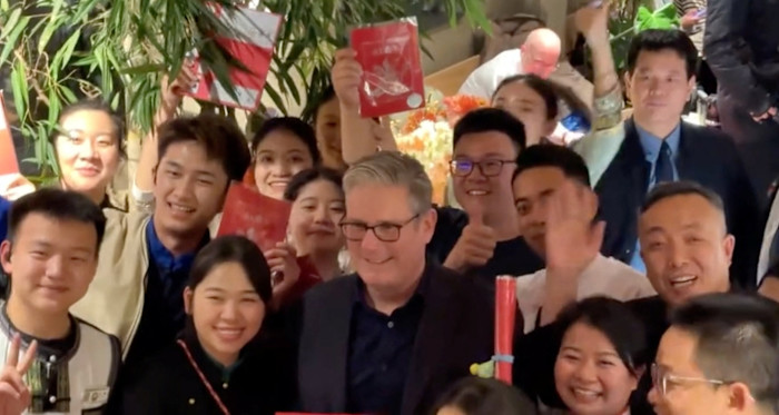 Keir Starmer smiles and poses with a group of restaurant staff, some holding red gift envelopes, in Beijing.