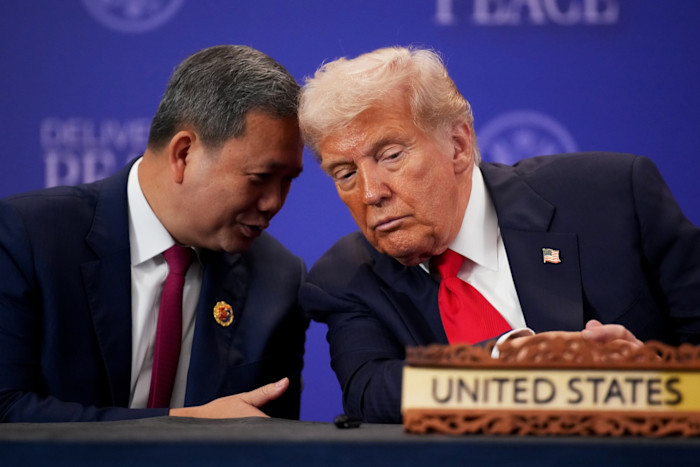 Cambodian Prime Minister Hun Manet leans in to speak to Donald Trump as they sit together at a table, with a United States nameplate in the foreground