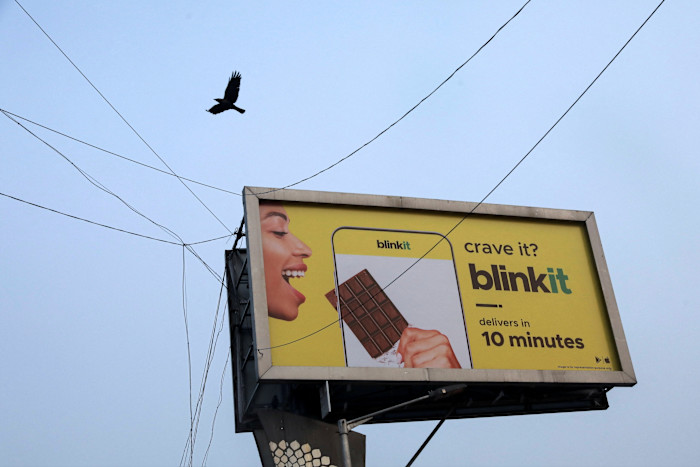 A bird flies over a hoarding featuring an advertisement of the SoftBank-funded Blinkit, an Indian company which is offering 10-minute deliveries for groceries, in New Delhi, India
