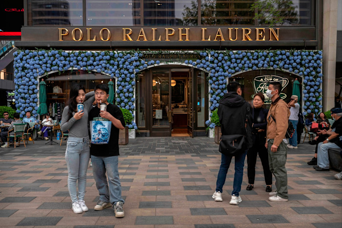 People stand and socialize outside the Polo Ralph Lauren store in Sanlitun, Beijing, with blue floral decorations around the entrance.