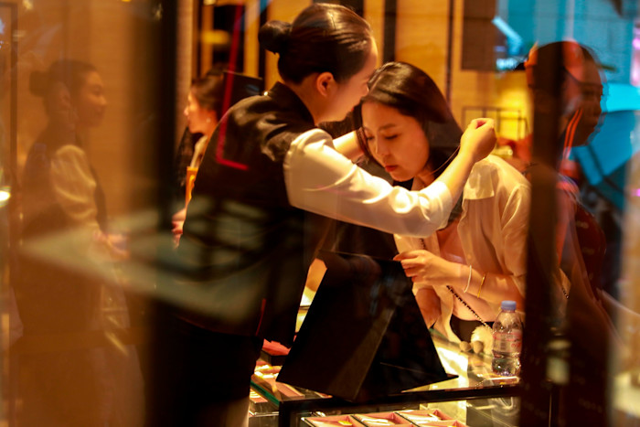 A shop assistant helps a customer try on a gold necklace at a jewelry counter inside Laopu Gold jewellery shop.