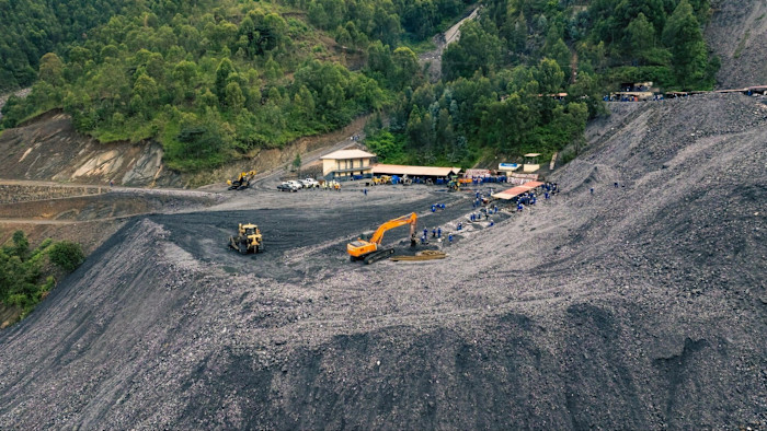 Aerial view of Nyakabingo Mine with mining equipment, buildings and numerous workers, surrounded by forested hills.